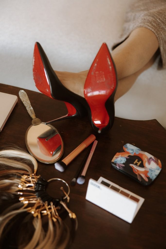 Costumography of memories - discarded mascara and high heels with an inviting warm bed in the background.